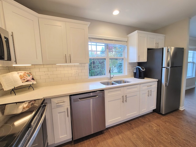 kitchen with stainless steel appliances, sink, decorative backsplash, white cabinetry, and hardwood / wood-style flooring