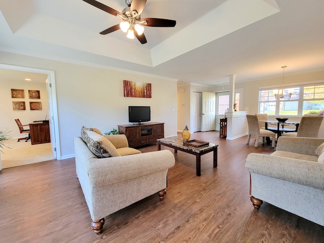 living room with crown molding, ceiling fan with notable chandelier, a tray ceiling, and hardwood / wood-style flooring