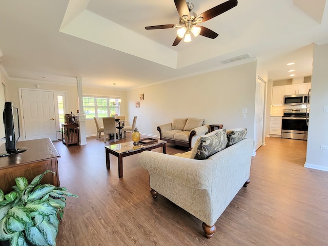 living room featuring hardwood / wood-style flooring, a tray ceiling, crown molding, and ceiling fan