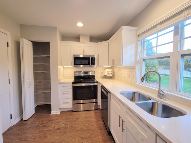 kitchen with stainless steel appliances, sink, backsplash, white cabinetry, and hardwood / wood-style flooring