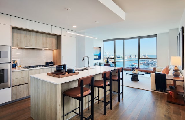 kitchen with a breakfast bar area, cooktop, tasteful backsplash, an island with sink, and dark wood-type flooring