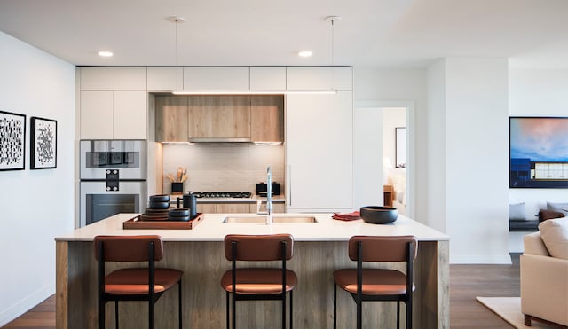 kitchen featuring decorative backsplash, dark wood-type flooring, a kitchen island with sink, and a kitchen bar