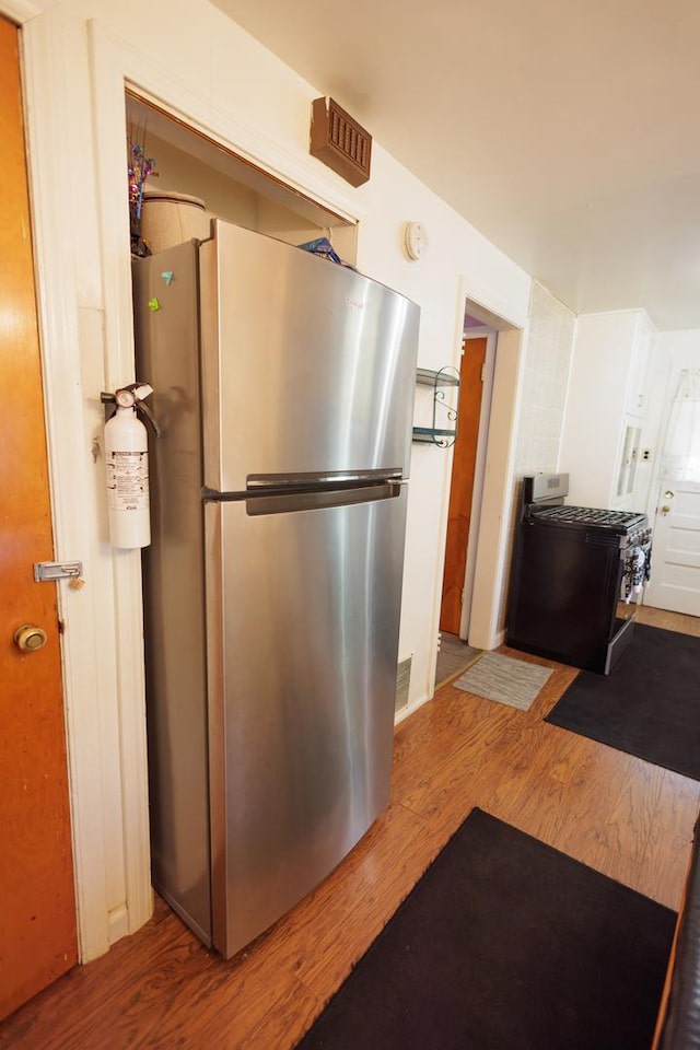 kitchen featuring stainless steel fridge, black range oven, and wood-type flooring