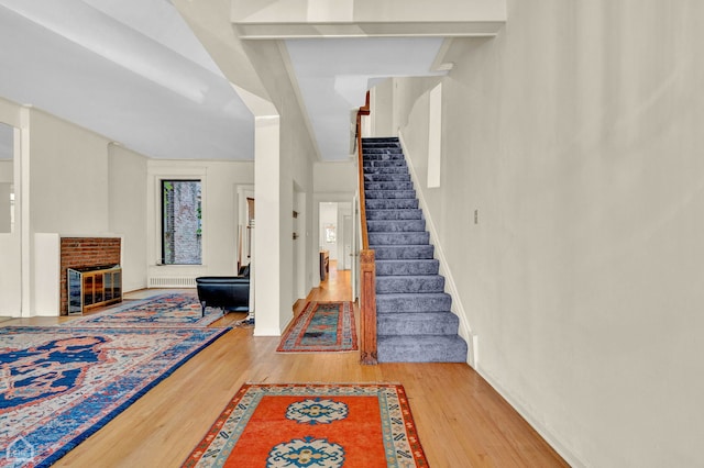 staircase with a fireplace, wood-type flooring, and vaulted ceiling with beams