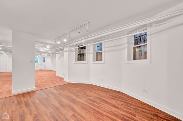 basement featuring rail lighting and hardwood / wood-style floors