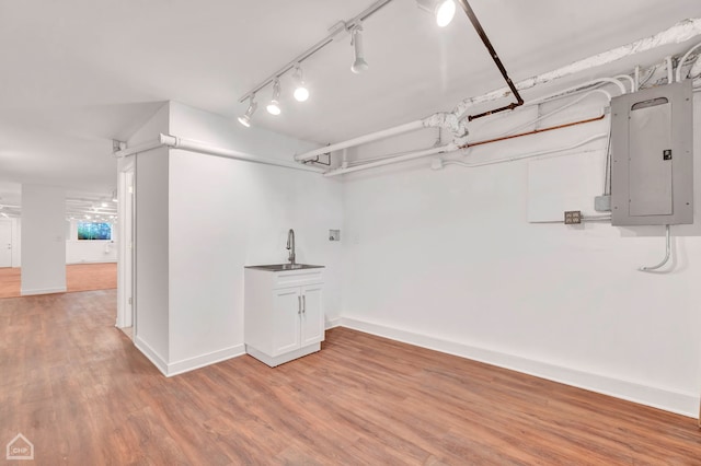 basement featuring light hardwood / wood-style floors, sink, electric panel, and track lighting