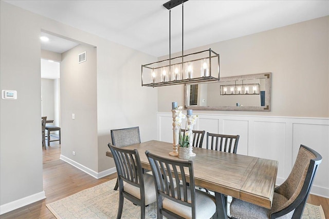 dining room featuring visible vents, a decorative wall, wood finished floors, and wainscoting