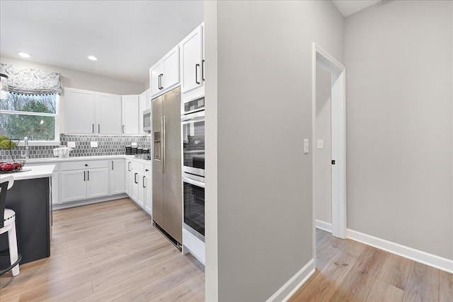 kitchen featuring tasteful backsplash, baseboards, white cabinets, light countertops, and light wood-style floors