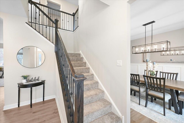 staircase with an inviting chandelier, baseboards, and wood finished floors