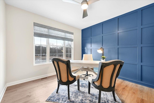 office area featuring ceiling fan, a decorative wall, visible vents, baseboards, and light wood finished floors