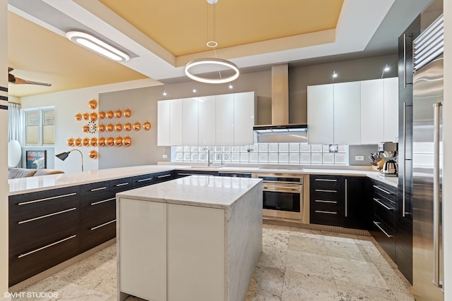 kitchen featuring appliances with stainless steel finishes, hanging light fixtures, a center island, white cabinetry, and wall chimney exhaust hood