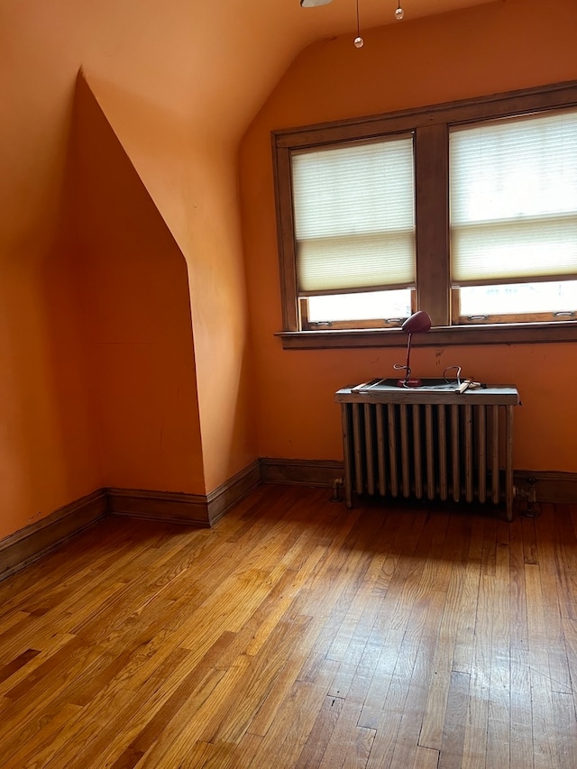 additional living space featuring vaulted ceiling, wood-type flooring, and radiator