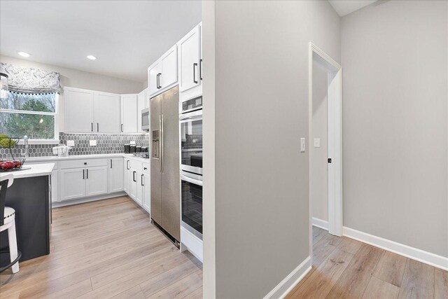 kitchen with light countertops, backsplash, white cabinets, light wood-type flooring, and baseboards