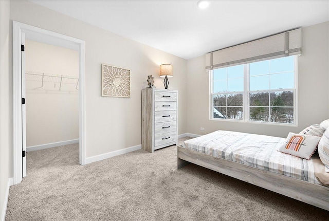 bedroom featuring a walk in closet, light carpet, and baseboards