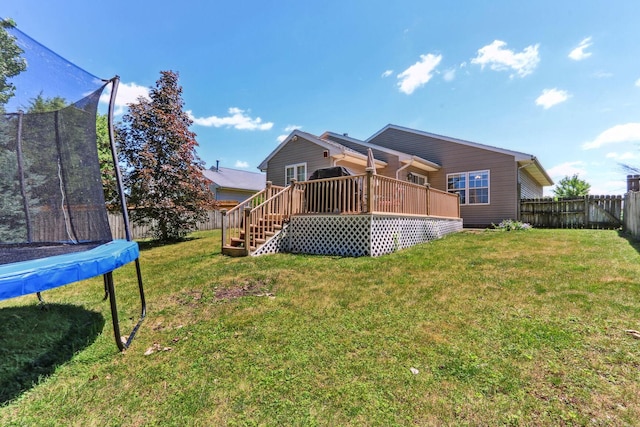 rear view of house featuring a lawn, a deck, and a trampoline