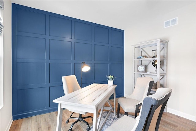 home office with baseboards, light wood-style floors, visible vents, and a decorative wall