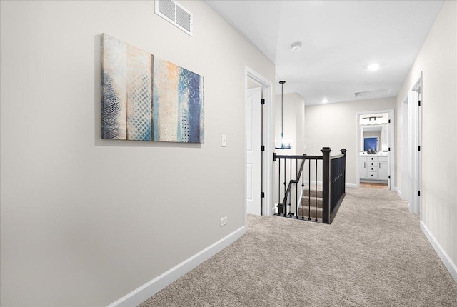 hall featuring light colored carpet, baseboards, visible vents, and an upstairs landing