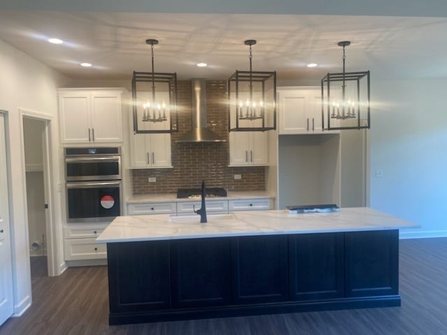 kitchen featuring pendant lighting, tasteful backsplash, an island with sink, and wall chimney exhaust hood