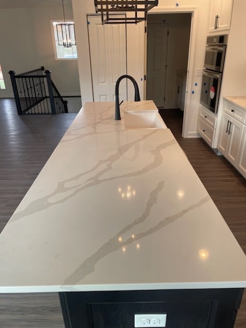 kitchen featuring stainless steel double oven, dark hardwood / wood-style floors, hanging light fixtures, and an island with sink