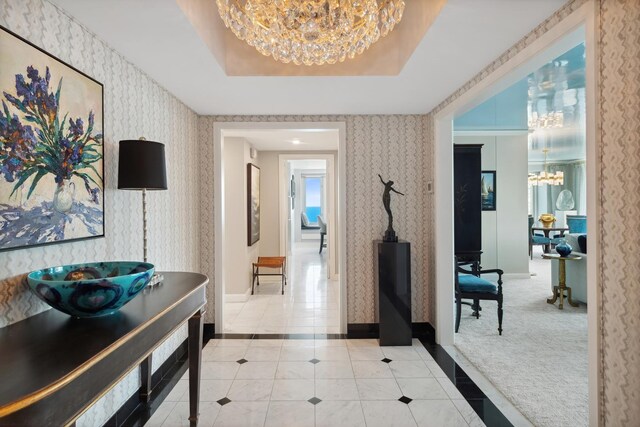 hall featuring light carpet, a tray ceiling, and a chandelier