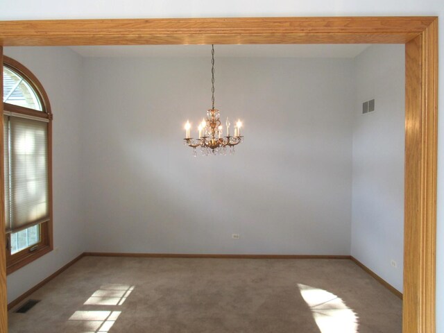 carpeted empty room with an inviting chandelier