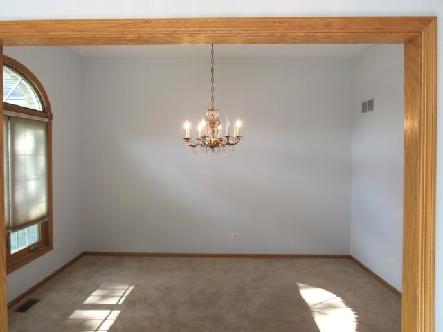 carpeted empty room with a notable chandelier