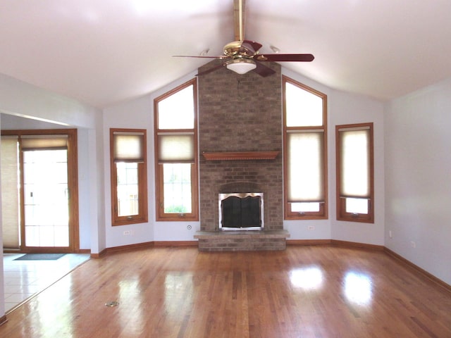 unfurnished living room featuring ceiling fan, brick wall, hardwood / wood-style flooring, and a brick fireplace