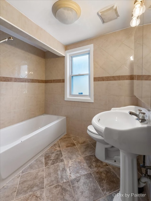 bathroom with tiled shower / bath combo, toilet, tile patterned floors, and tile walls