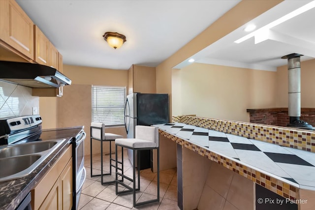 kitchen with fridge, backsplash, light tile patterned floors, stainless steel electric range oven, and light brown cabinetry