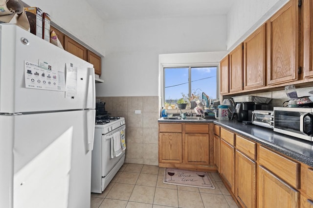 kitchen with white appliances, tile walls, wall chimney exhaust hood, sink, and light tile patterned flooring