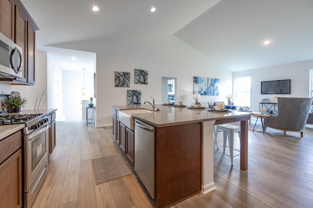 kitchen with an island with sink, appliances with stainless steel finishes, open floor plan, vaulted ceiling, and light wood-style floors