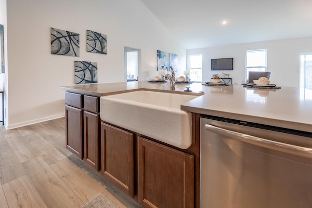 kitchen featuring lofted ceiling, light wood-style flooring, a sink, baseboards, and stainless steel dishwasher