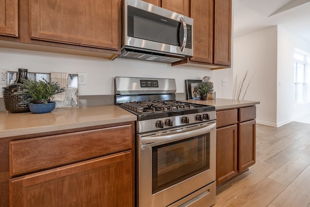 kitchen with stainless steel appliances, brown cabinetry, light countertops, and light wood-style flooring