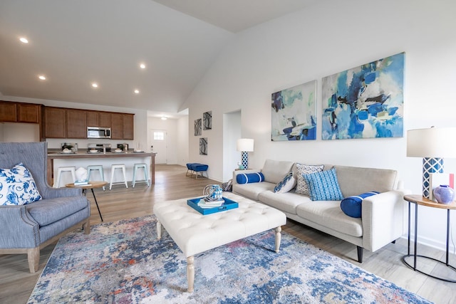 living area featuring high vaulted ceiling, light wood-style flooring, and recessed lighting