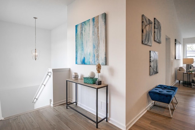 corridor with an inviting chandelier, light wood-type flooring, an upstairs landing, and baseboards