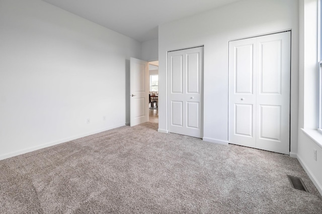 unfurnished bedroom featuring two closets, carpet flooring, visible vents, and baseboards