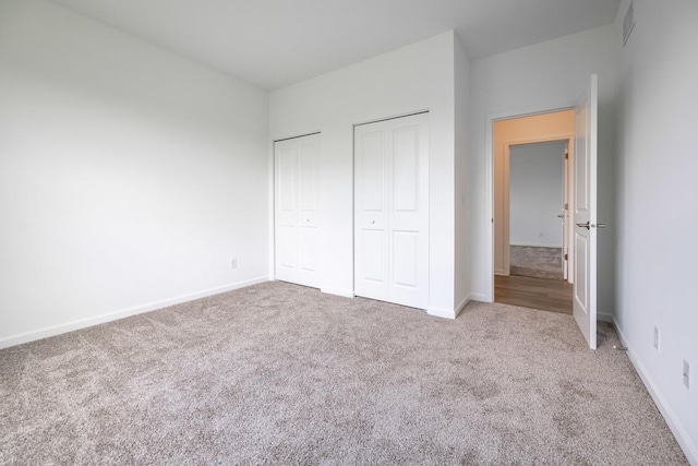 unfurnished bedroom with carpet floors, visible vents, baseboards, and two closets