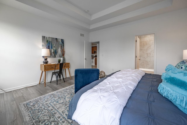 bedroom featuring baseboards, visible vents, a raised ceiling, wood finished floors, and ensuite bathroom