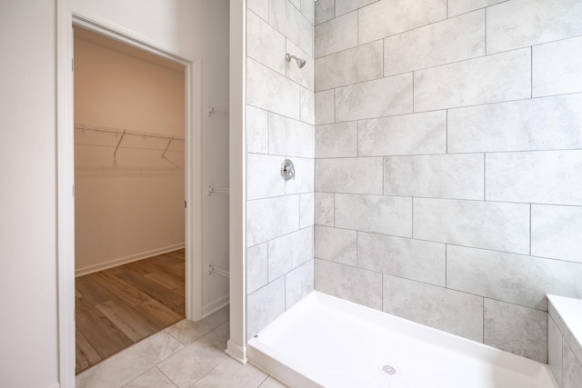 full bathroom with a stall shower, a spacious closet, baseboards, and tile patterned floors