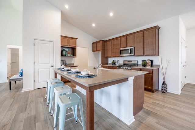 kitchen with light wood-style flooring, stainless steel appliances, light countertops, brown cabinetry, and an island with sink