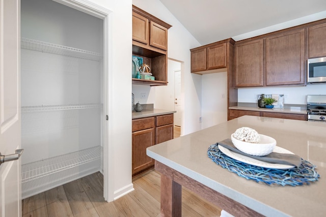 kitchen with stove, light countertops, light wood-type flooring, brown cabinets, and stainless steel microwave