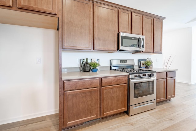 kitchen with stainless steel appliances, light countertops, brown cabinetry, light wood-style floors, and baseboards