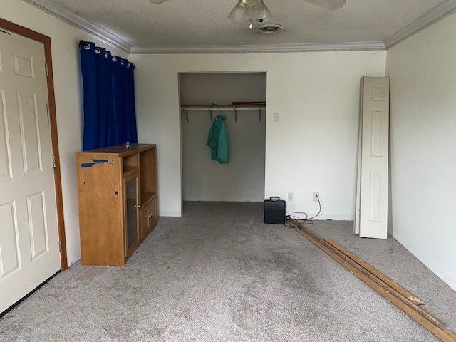 unfurnished bedroom with carpet flooring, a closet, ceiling fan, and crown molding