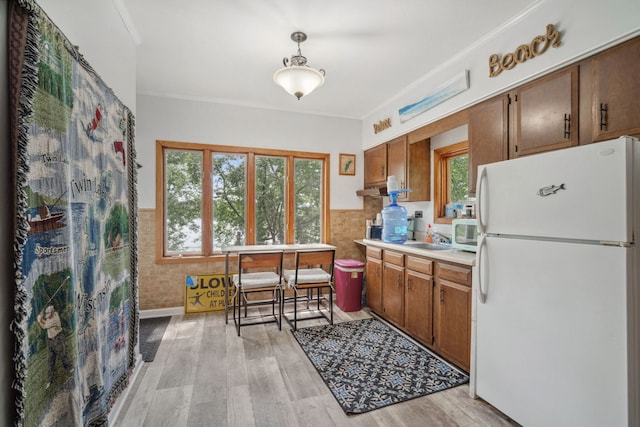 kitchen with white appliances, wainscoting, light wood-style flooring, light countertops, and crown molding