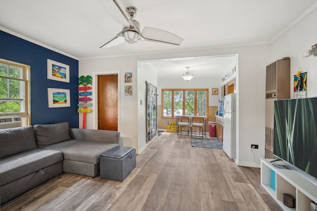 living area with baseboards, wood finished floors, a ceiling fan, and crown molding