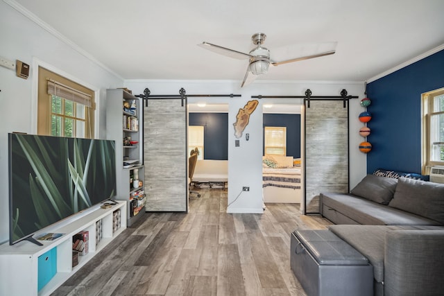 living area with a barn door, crown molding, ceiling fan, and wood finished floors