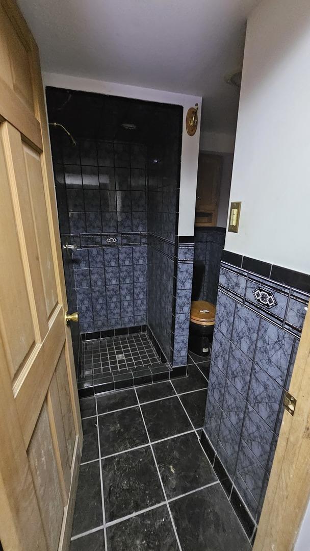 full bathroom with tile walls, toilet, wainscoting, a shower stall, and tile patterned floors