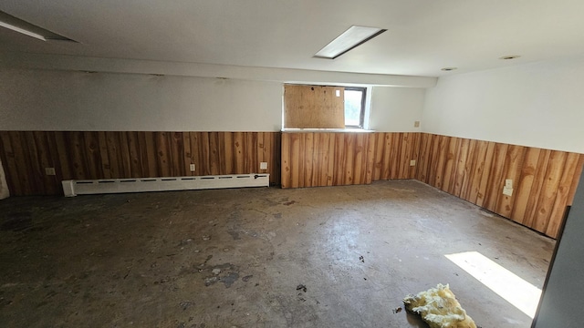 unfurnished room featuring wooden walls, a baseboard heating unit, and wainscoting