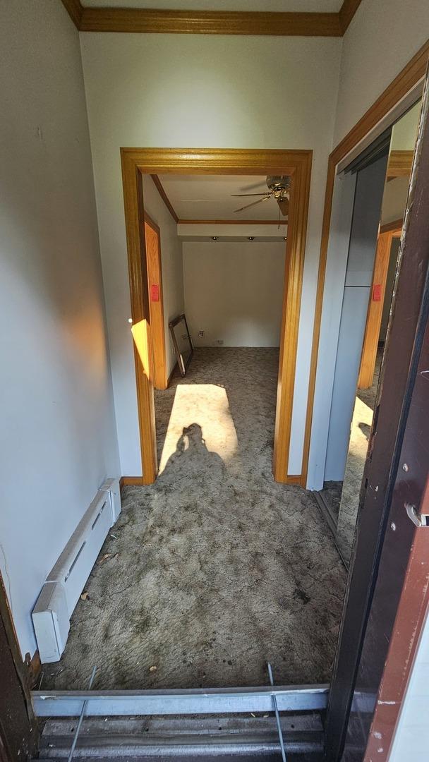 hallway with ornamental molding, baseboard heating, and carpet flooring