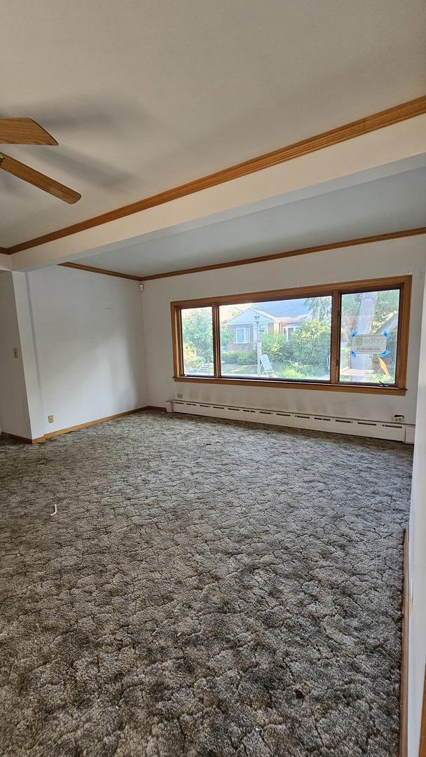 carpeted empty room featuring a baseboard heating unit and a ceiling fan